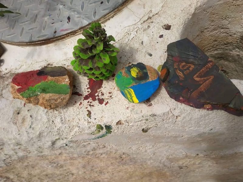 حجارة لوّنها الأطفال بألوان الجواش خلال لقاء من برنامج هيا بنا نقرأ، تُركت لتجف على حافة حجرية.